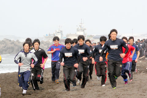 サンセットビーチ砂浜を走るラグビー部員の写真